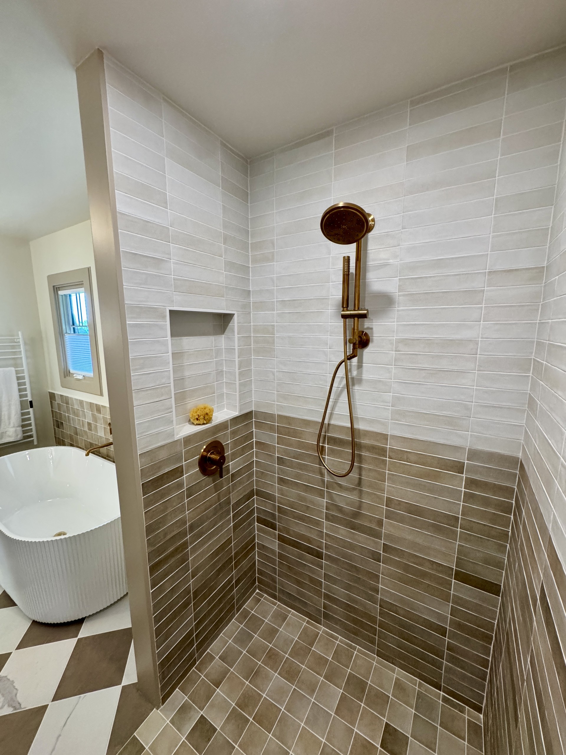 Two-toned tile shower with bronze fixtures and a freestanding tub, by CB Built Homes